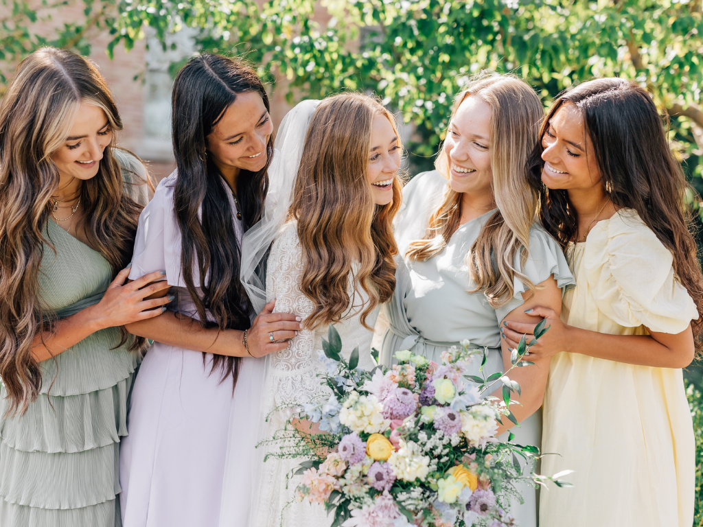 A bride laughing with her bridesmaids, holding a pastel wedding bouquet